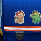 Reflektierende Aufkleber Stoff Textil  Katze „Miez“ und Krokodil „Freddy“ aus der Produktserie „Reflective Friends“  die auf einen blauen Schulrucksack geklebt in Detailansicht. Von REFLECTIVE Berlin.