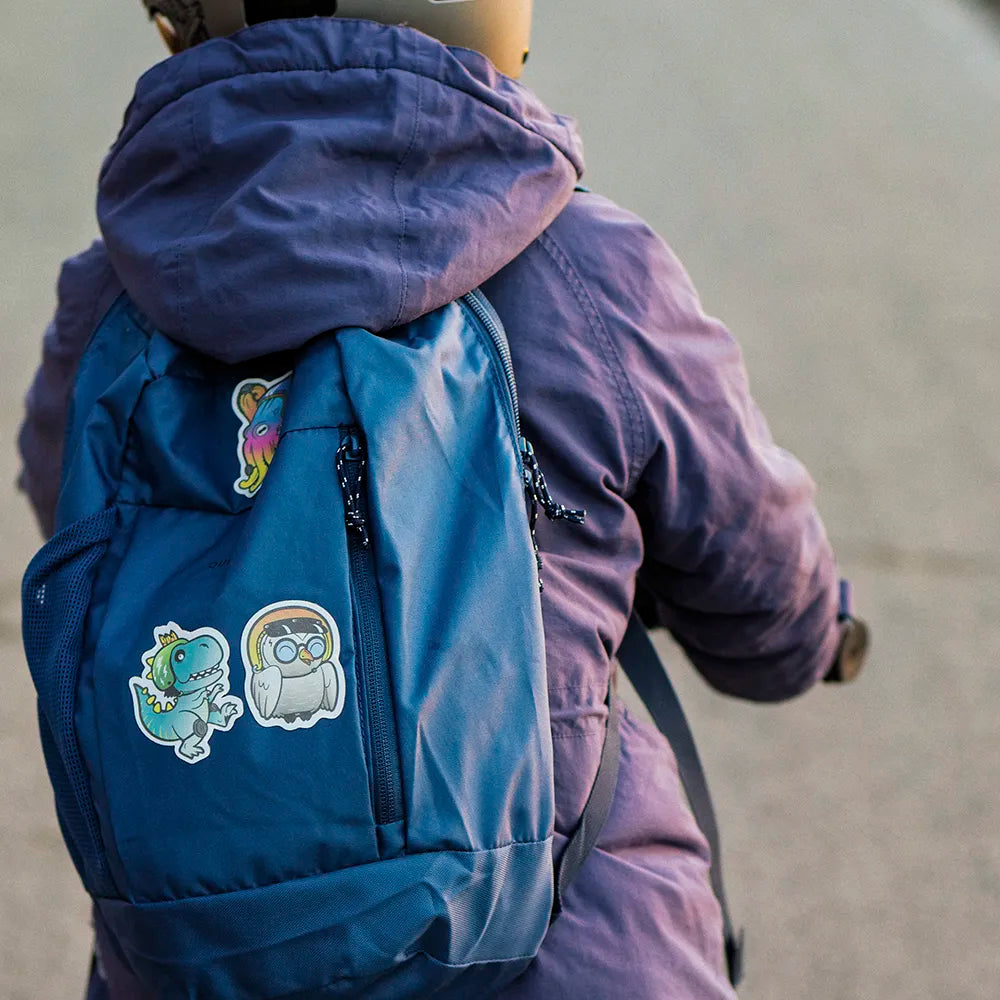 Reflektierende Aufkleber Sticker Stoff Textil Oktopus „Otto“ , Dinosaurier T-Rex „Lino“ und Eule „Olli“ aus der Produktserie „Reflective Friends“  die auf einen blauen Rucksack kleben, der von einem Kind auf einem Roller getragen wird. Von REFLECTIVE Berlin.