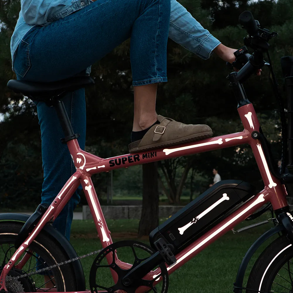Jemand stellt sein rechtes Bein auf das Oberroh vom Super Mini Bike mit reflektierenden Knochen Stickern