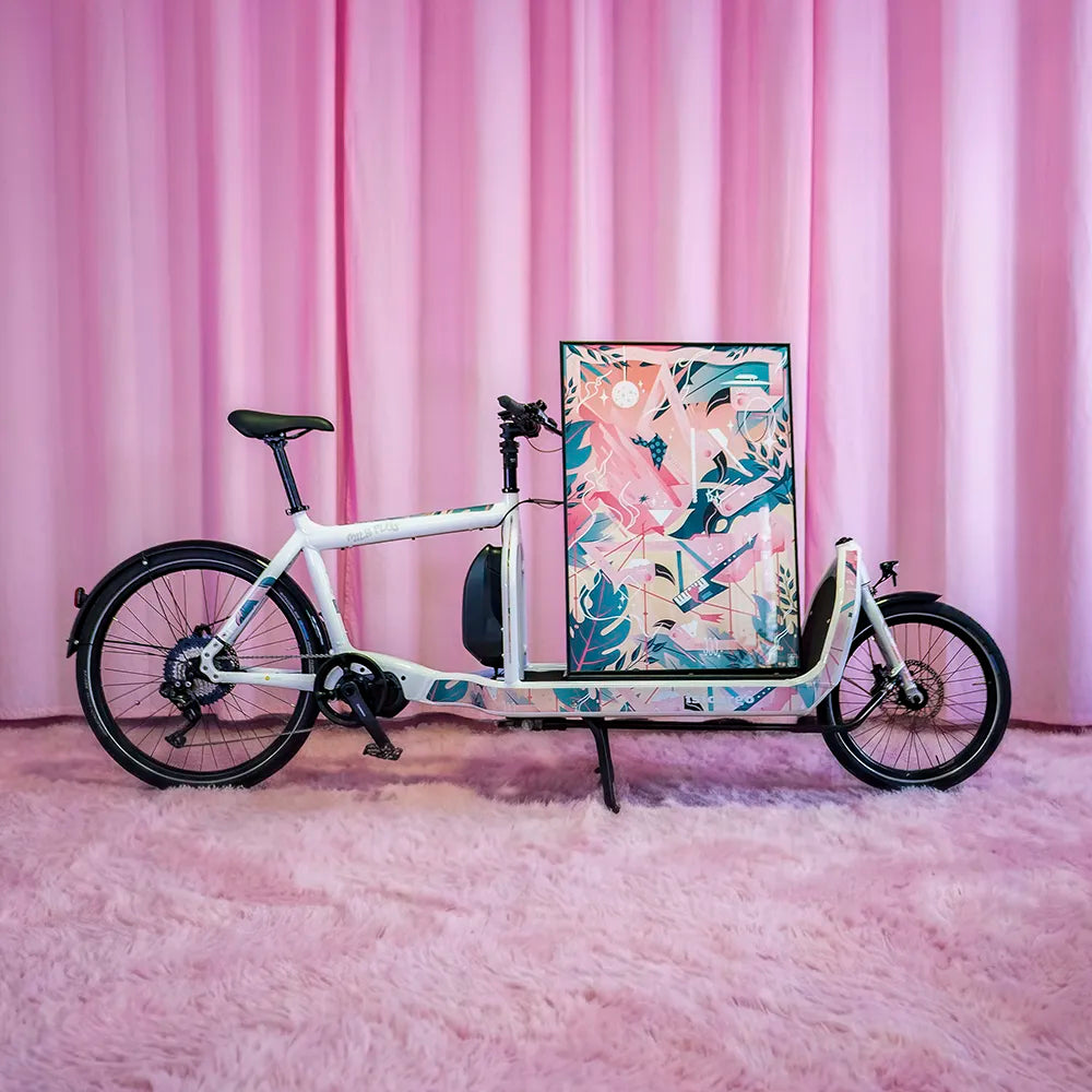 Reflektierende Aufkleber Folie XXL „Flamingo Funk“ als Posterformat und zugeschnitten und auf einem BULLITT „Milk Plus“ Lastenrad aufgeklebt.  Das BULLITT Cargo Fahrrad ist im Profil zu sehen vor einem rosa Vorhang. Das gerahmte Flamingo Funk Poster steht auf der Tragfläche vom Lastenrad. Das Arrangement ist von REFLECTIVE Berlin.