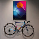 Reflektierende Aufkleber Folie XXL „Venus“ mit abstrakten Formen in Blauen, orangen und pinken Farbtönen, in Bilderrahmen, der über einem Rennrad an der Wand hängt. Das Rennrad ist mit zugeschnittenen Sticker Elementen aus der Aufkleber Folie beklebt. Arrangement von REFLECTIVE Berlin.