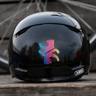 Zwei Reflektierendee Aufkleber „Berliner Bär“ in Farbvariante „Regenbogen“ zugeschnitten auf schwarzem Fahrradhelm Rückansicht. Von REFLECTIVE Berlin.