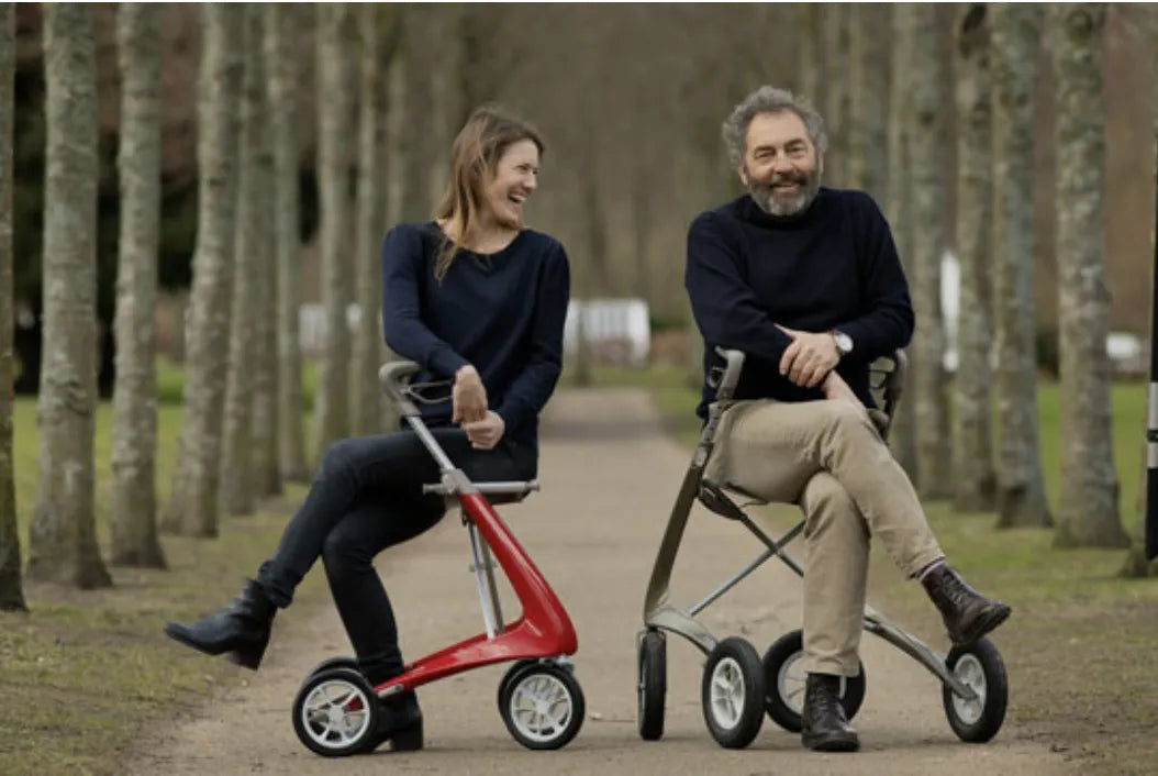 Gründer und CEO von byacre sowie eine lachende Mitarbeiterin sitzen jeweils auf einem Rollator in einer Allee
