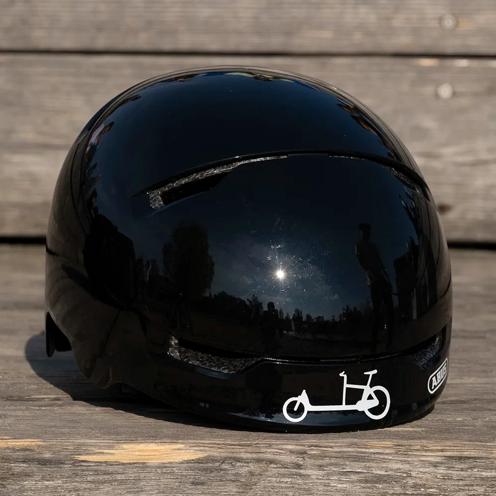 Reflektierender Aufkleber „Cargo“ in Farbvariante „weiß“ auf schwarzem Fahrradhelm Frontansicht vor unscharfem Hintergrund von REFLECTIVE Berlin.
