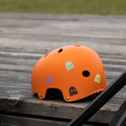 Reflektierender Aufkleber „Geister“ in Farbvariante „Eiscreme“   und „Schwarz“ auf orangenem Fahrradhelm in Seitenansicht mit verschwommenen Hintergrund von REFLECTIVE Berlin.