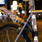 Reflektierender Aufkleber „Geister“ in Farbvariante „weiß“  auf silbernen Fahrradrahmen mit verschwommenen Hintergrund  und Straßenlichtern von REFLECTIVE Berlin.