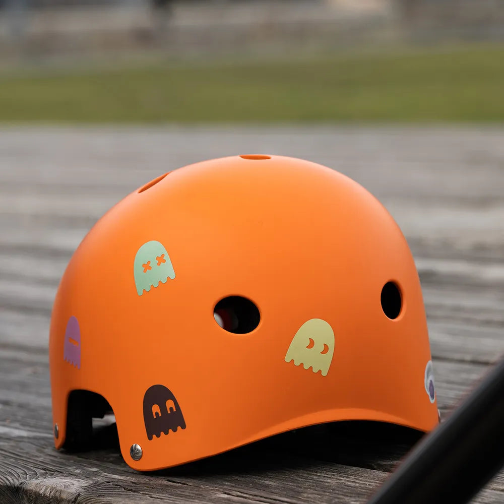 Reflektierender Aufkleber „Geister“ in Farbvariante „Icecream“ und „schwarz“  auf orangem Fahrradhelm mit verschwommenen Hintergrund von REFLECTIVE Berlin.