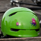 Reflektierender Aufkleber „Oktopus“ in Farbvariante „Neptun“ auf grünen Fahrradhelm vor unscharfem Hintergrund Frontansicht. Von REFLECTIVE Berlin.