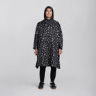 reflektierender Fahrrad Regenponcho in Farbvariante „Doodle“ getragen von einer Person, die frontal in die Kamera schaut vor weißem Hintergrund. Kollaboration von Bomance und REFLECTIVE Berlin.