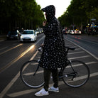 reflektierender Fahrrad Regenponcho in Farbvariante „Doodle“ getragen von einer Person, die einen Fahrradhelm trägt und auf dem Mittelstreifen einer Straße steht. Kollaboration von Bomance und REFLECTIVE Berlin.