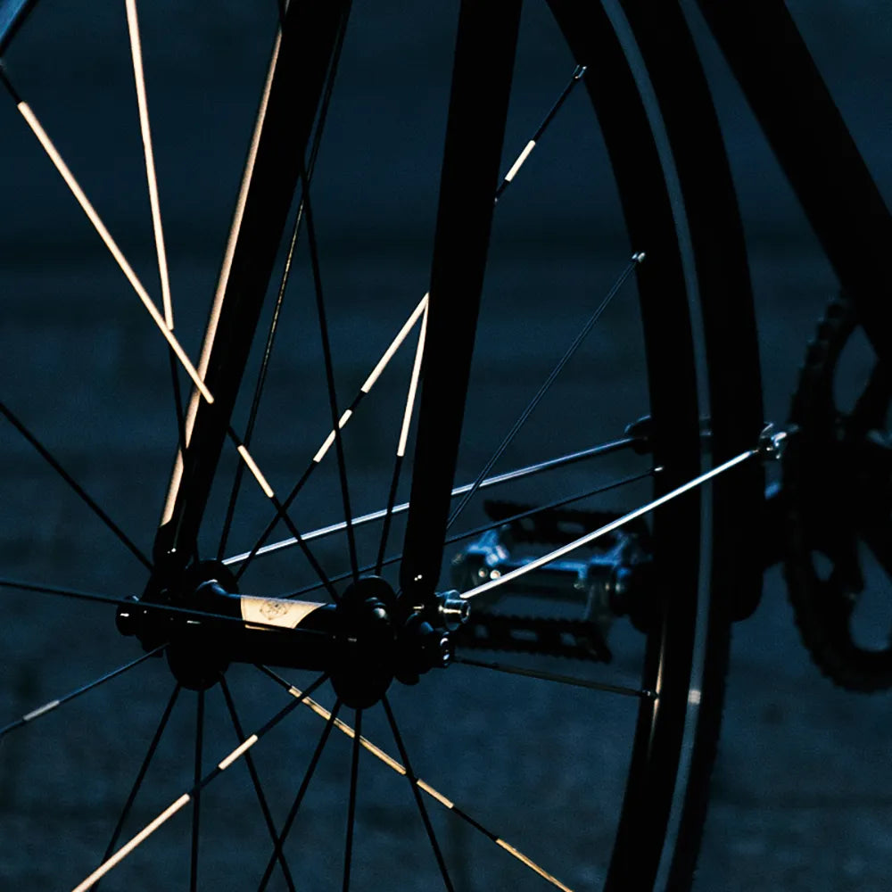 Reflektierender Speichen Aufkleber „Spokes“ in Farbvariante „weiß“ auf den Speichen von einem Vorderrad eines Fahrrads. Blitzlicht hebt die Reflexion hervor. Von REFLECTIVE Berlin.