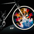 Reflektierender Speichen Aufkleber „Spokes“ in Farbvarianten „weiß“, „Regenbogen“, „Feuer" auf den Speichen von einem rotierenden Vorderrad eines Fahrrads. Blitzlicht hebt die Reflexion hervor. Von REFLECTIVE Berlin.