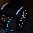 Reflektierender Speichen Aufkleber „Spokes“ in Farbvariante „weiß“ auf den Speichen von einem Rollstuhl. Auf dem Rahmen sind reflektierende Aufkleber „DIY“ in Farbvariante „vitrail“ verklebt.  Von REFLECTIVE Berlin.