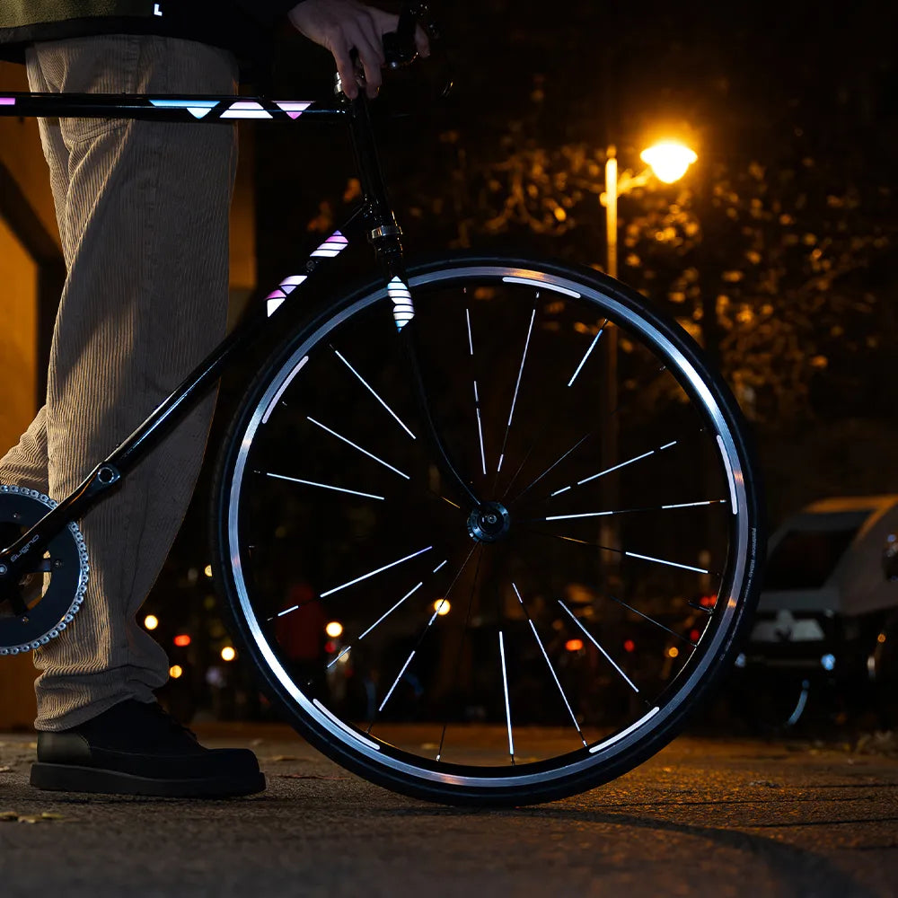 Reflektierender Speichen Aufkleber „Spokes“ in Farbvariante „weiß“ auf den Speichen von einem Vorderrad eines Fahrrads. Blitzlicht hebt die Reflexion hervor. Auf dem Fahrradrahmen und Gabel kleben reflektierende Aufkleber „Delta“, Farbvariante „Spacebaby“ von REFLECTIVE Berlin.