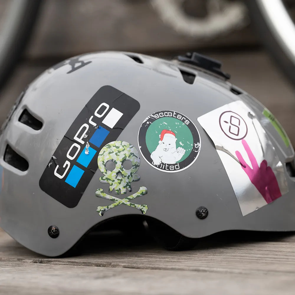 Reflektierender Aufkleber „Totenkopf“ in Farbvariante „Camo“ auf grauen Fahrradhelm mit weiteren Stickern. von REFLECTIVE Berlin.