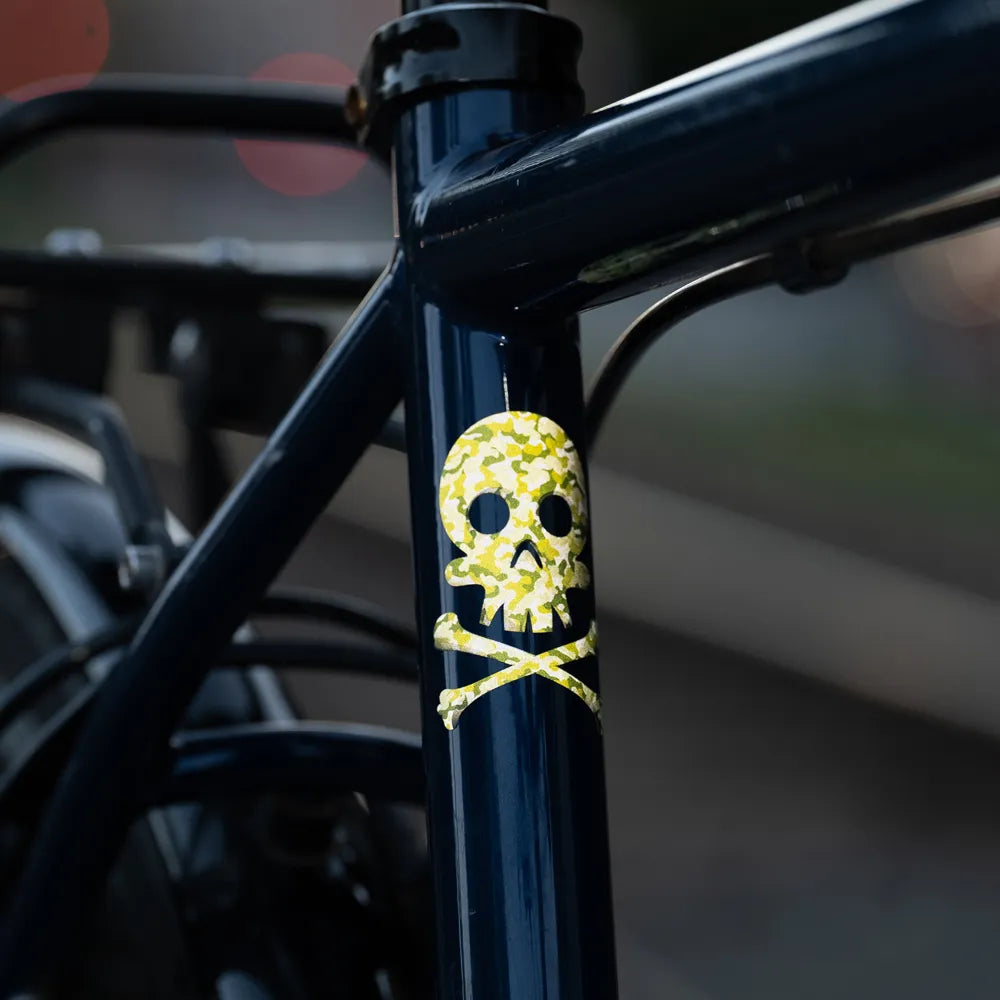 Reflektierender Aufkleber „Totenkopf“ in Farbvariante „Camo“ auf schwarzem Fahrradrahmen. Von REFLECTIVE Berlin.