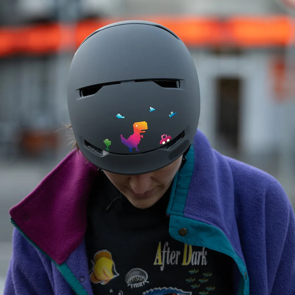 Reflektierender Aufkleber „T-Rex“ in Farbvariante „Regenbogen“ auf Fahrradhelm, der von einer Person getragen wird. Von REFLECTIVE Berlin.