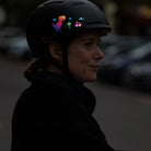 Reflektierender Aufkleber „T-Rex“ in Farbvariante „Regenbogen“ auf schwarzem Fahrradhelm der von einer Person getragen wird. Von REFLECTIVE Berlin.