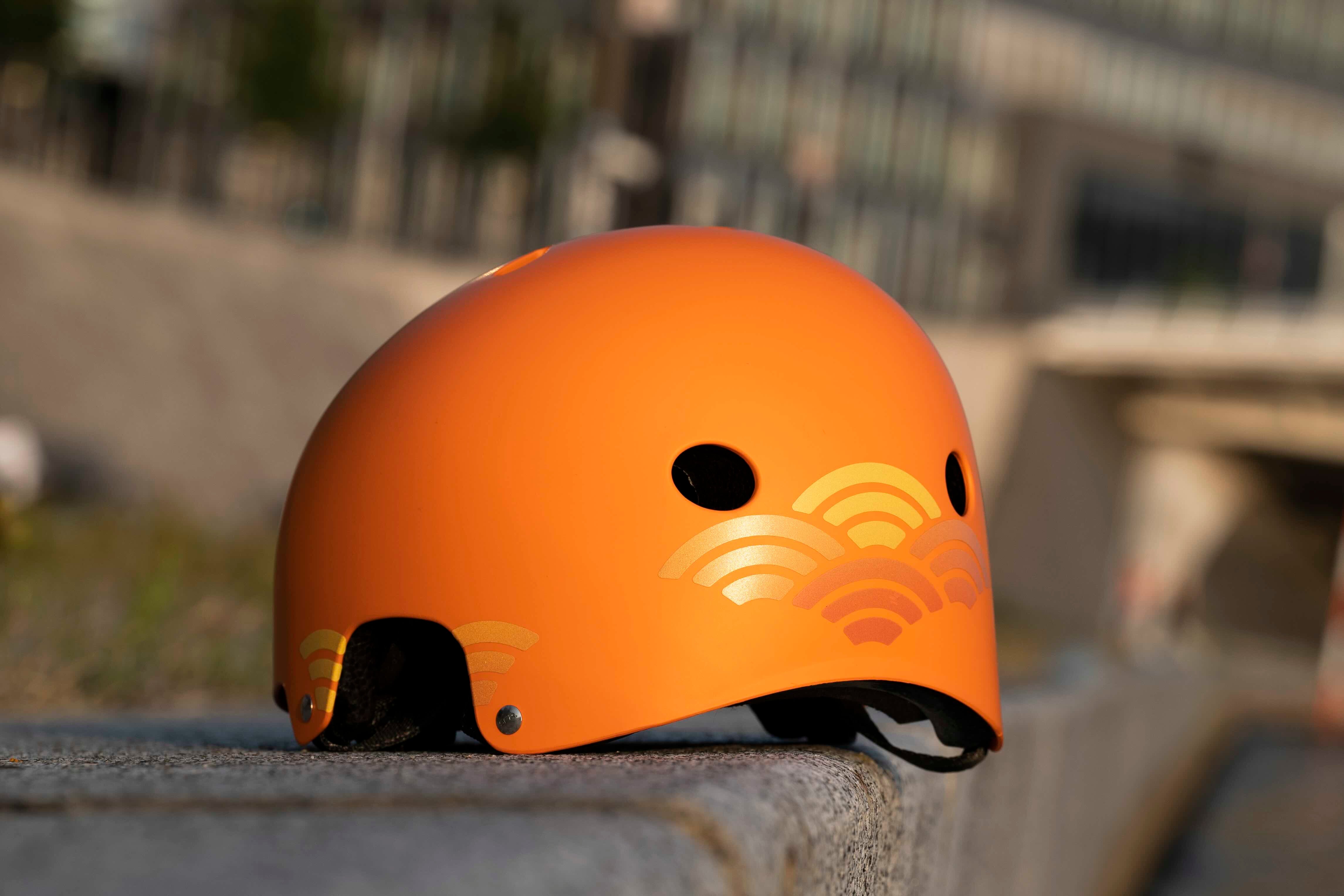 Sunrise Orange von REFLECTIVE Berlin auf orangem Fahrradhelm mit stark reflektierenden Linienformen für mehr Sichtbarkeit im urbanen Stil.