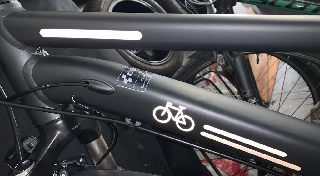 Universal White und Bicycle White von REFLECTIVE Berlin auf schwarzem Fahrradrahmen mit stark reflektierenden weißen Linien- und Schriftformen für mehr Sichtbarkeit im urbanen Stil.