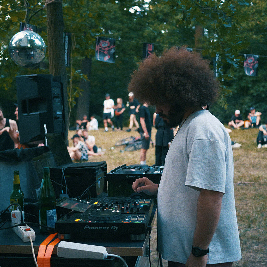 Seitliche Ansicht von Mann mit Afrofrisur im Park, der als DJ einen Controller bedient