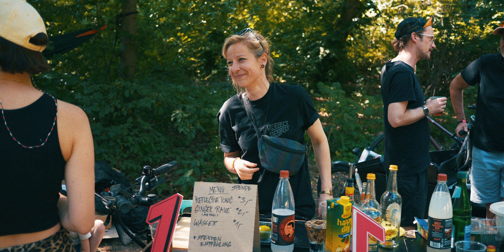 Frau im Park steht hinter einer selbst gebauten Bar und grinst