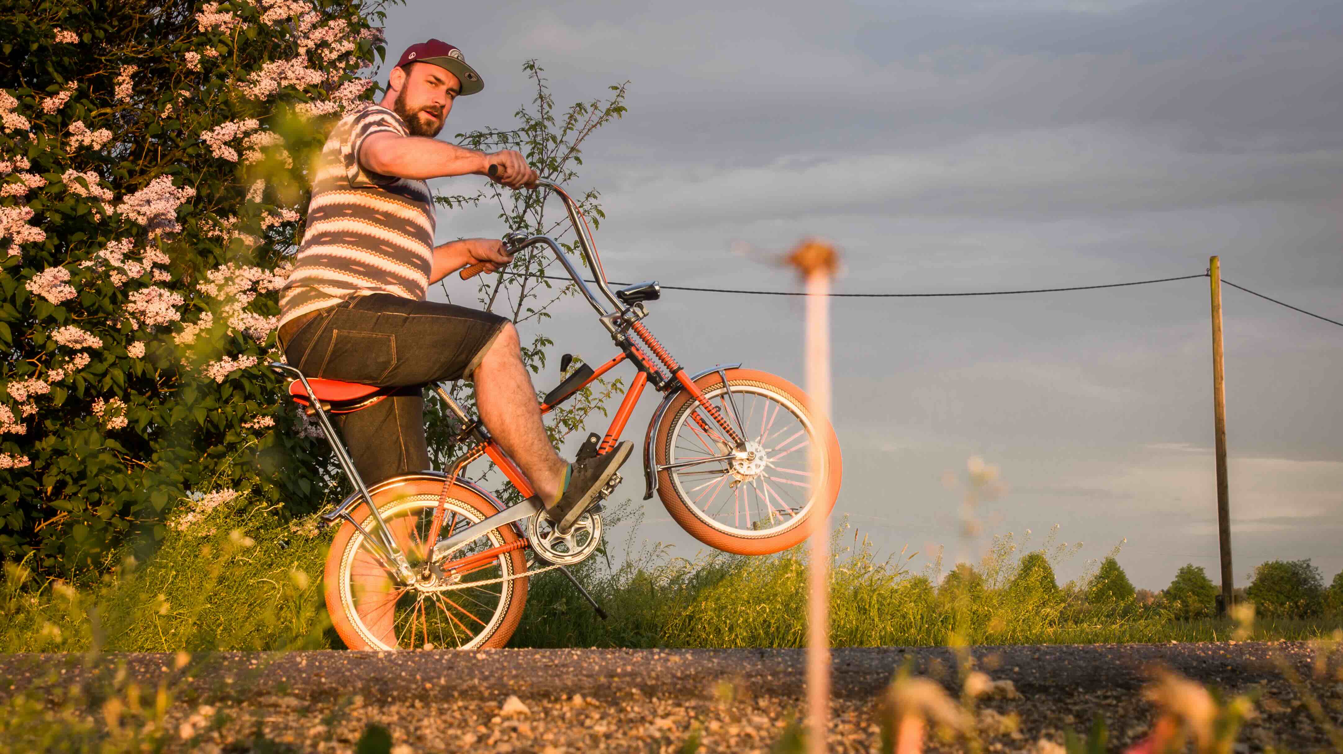 Mann mit orangenem Bonanza Fahrrad deutet einen Wheelie an und schaut in die Kamera