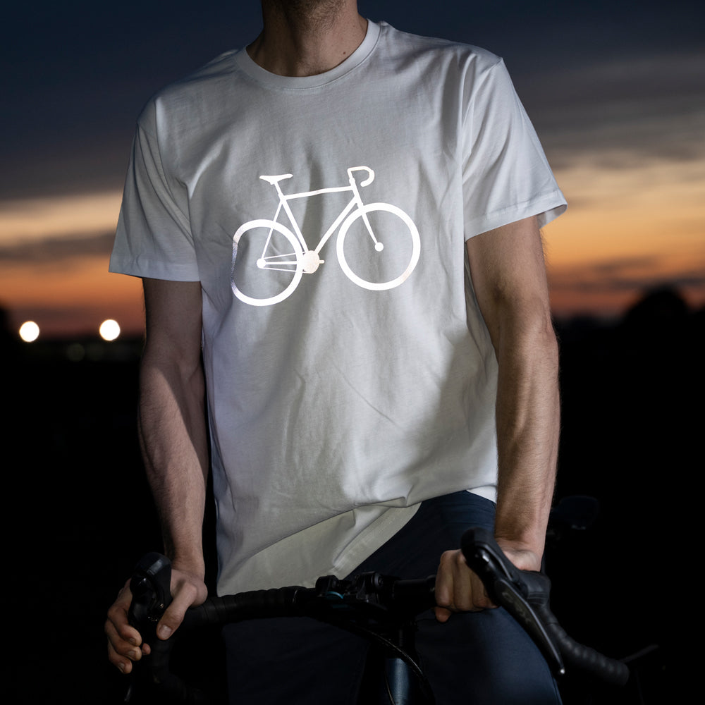 Typ mit weißem T-Shirt hält sein Fahrrad am Lenker, Fahrrad Print auf der Brust reflektiert hell in der Dunkelheit