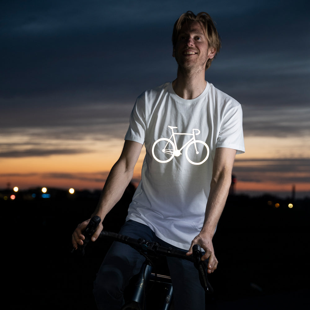 Fahrradfahrer vor Abendhimmel lacht und schaut in die Ferne, er trägt ein weißes T-Shirt mit Fahrrad Aufdruck