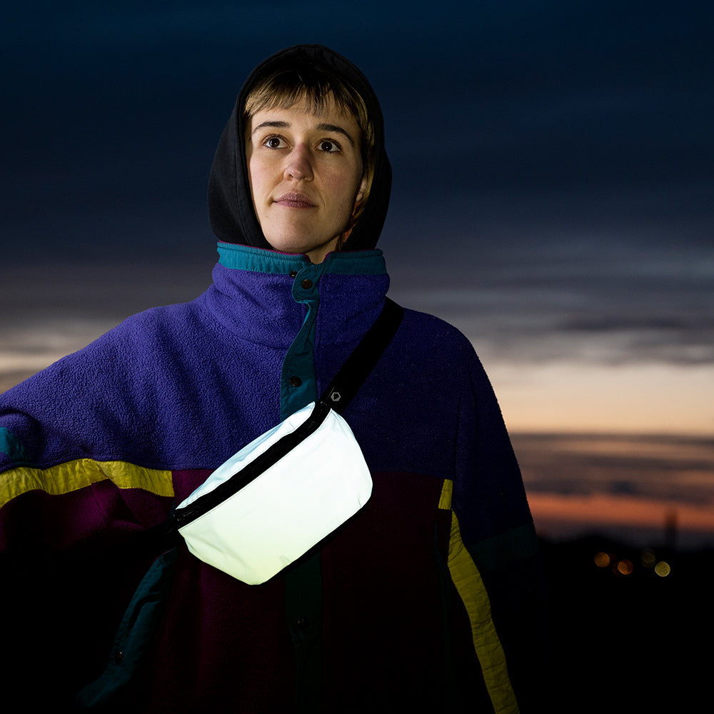 Girl with Hoodie in front of a colorful night sky wearing a reflective hipbag