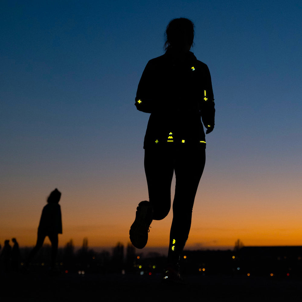 Frau läuft in den Sonnenuntergang, reflektierende Sticker auf Jacke und Hose machen sie sichtbar