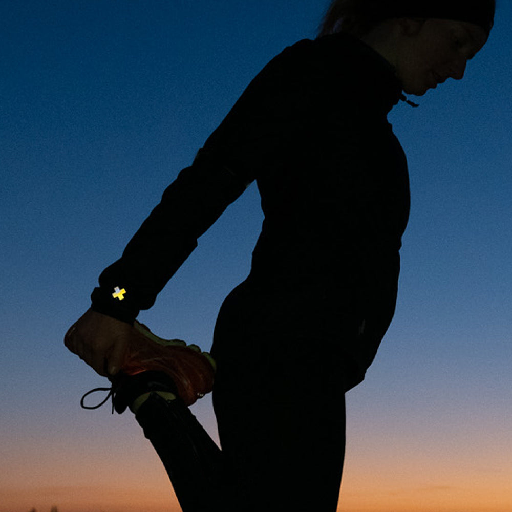 Joggerin strecht bei Sonnenuntergang nach dem Laufen, Reflektierender Aufkleber an Laufbekleidung