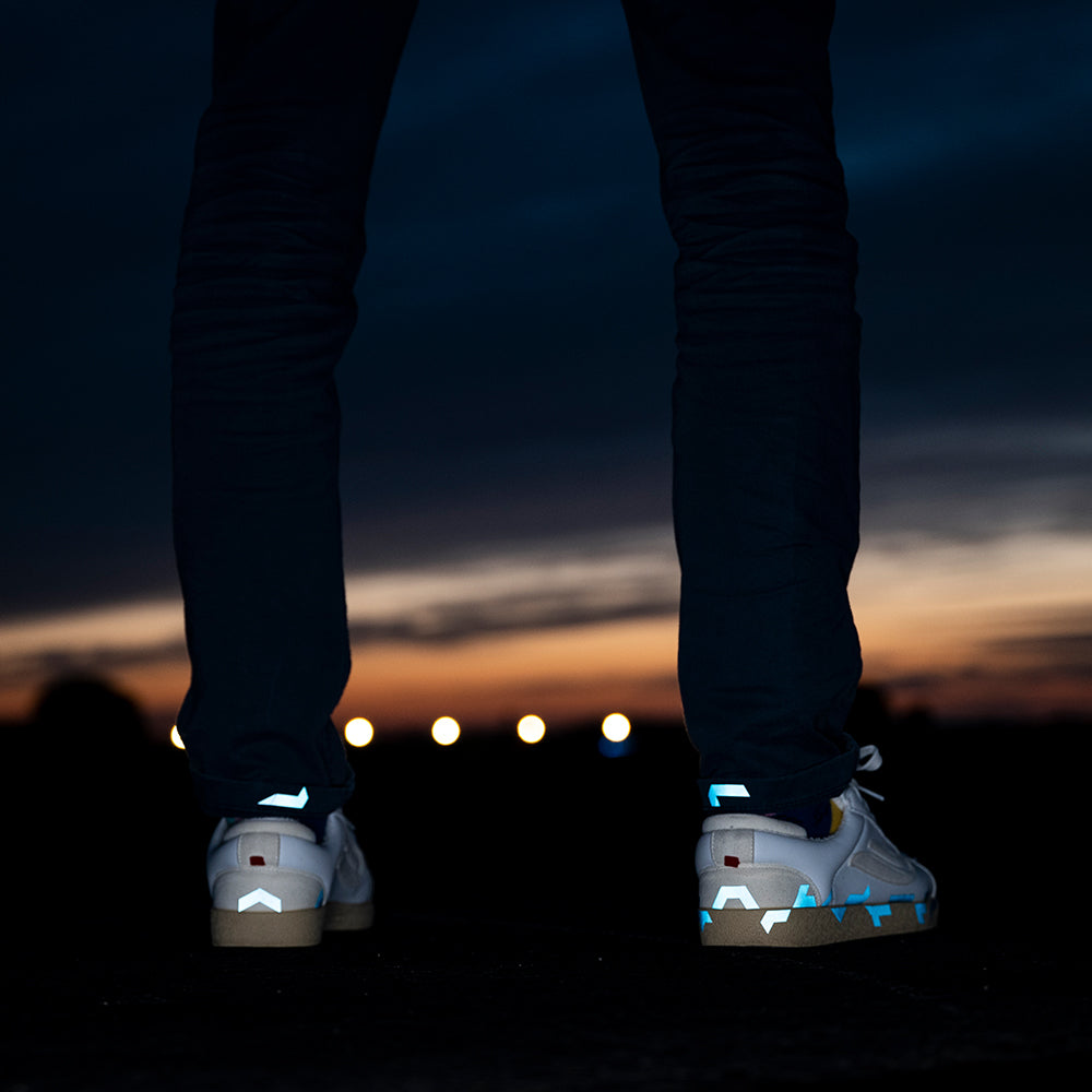 Beine einer stehenden Person vor weitem Abendhimmel, die Schuhe reflektieren teilweise