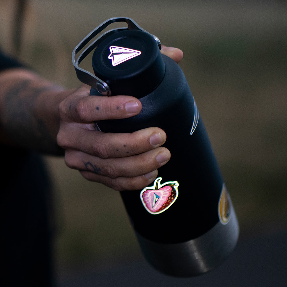 hand holding a metal water bottle with a reflective paperplane design 