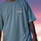 hellblaues T-Shirt mit bunt reflektierenden Streifen auf Brusthöhe, linker Arm ist tättowiert