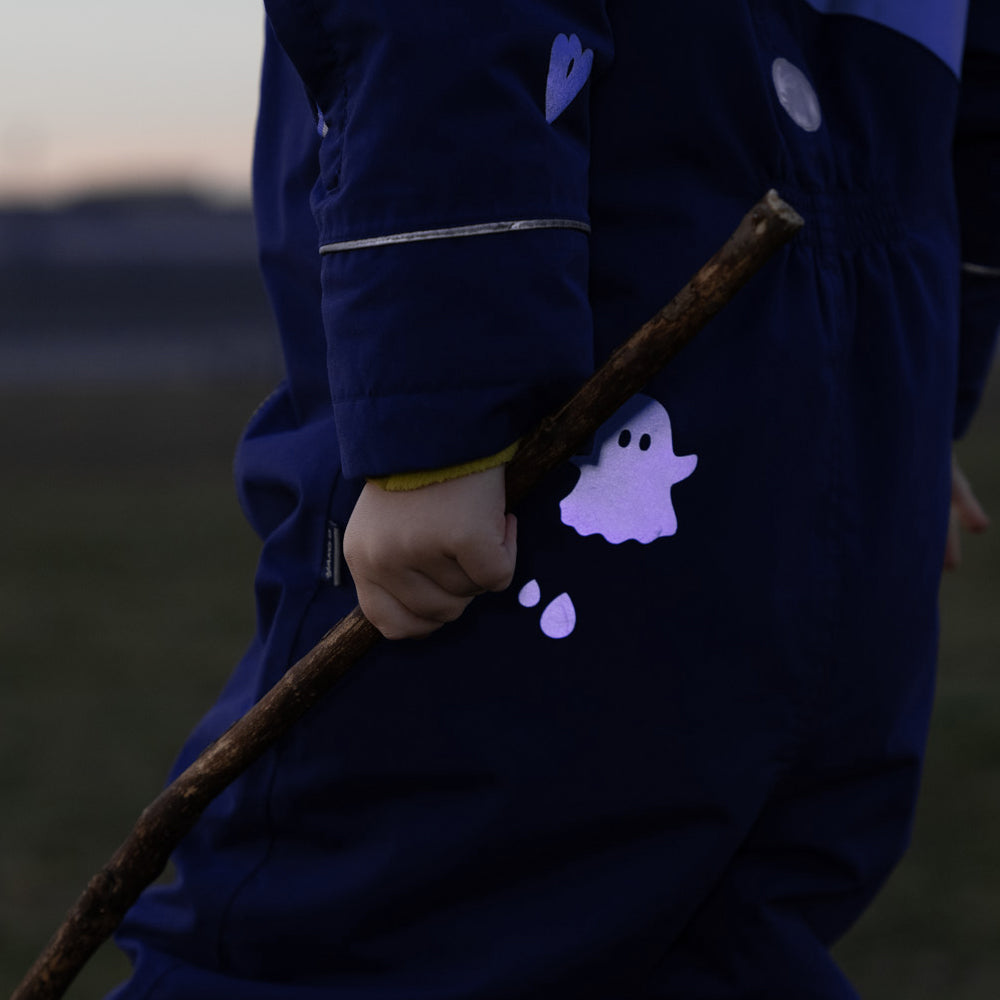Kind mit Stock in der linken Hand, trägt Schneeanzug und hat reflektierenden Geist Sticker auf der Kleidung