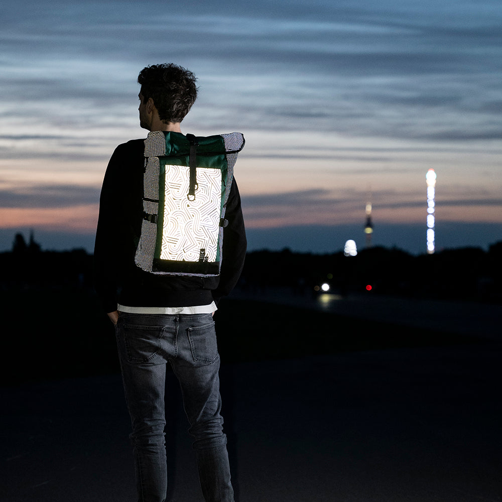 Mann auf weiter Ebene schaut in den Abendhimmel, trägt einen stark reflektierenden Rucksack auf dem Rücken