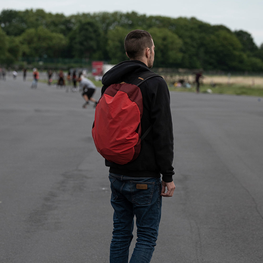 Typ mit rotem Rucksack steht im Park und guckt in die Weite