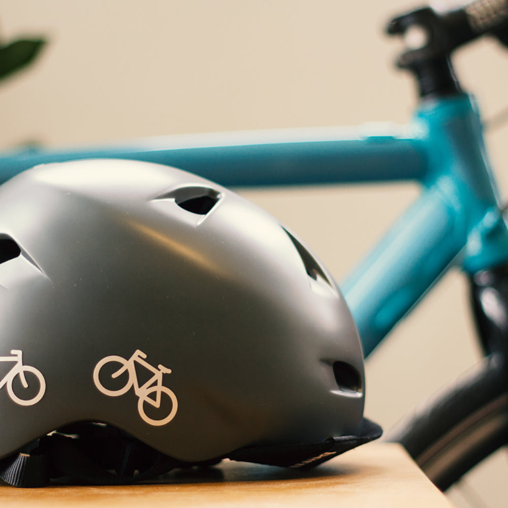grauer Bern Helm mit Fahrrad im Hintergrund, Seitenansicht, mit Fahrrad Aufklebern in weiß
