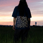 Frau steht im Gras, guckt in den Sonnentuntergang , ihr T-Shirt hat reflektierende Linien