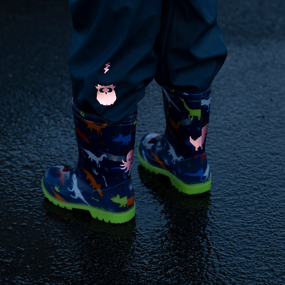 Kind mit Gummistiefeln auf nassem Boden, mit Reflexaufklebern auf Schuhen und Regenhose
