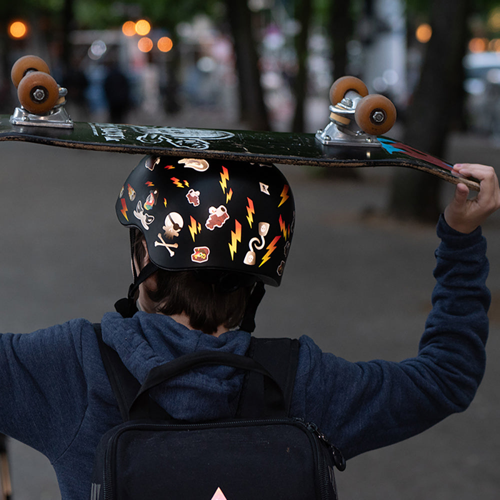 Jugendlicher mit Skateboard und Helm, reflektierende Aufkleber Blitze und Piraten orange
