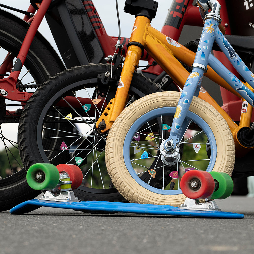 Drei Fahrräder hintereinander vor Skateboard, alle mit Aufklebern an Speichen und Rahmen
