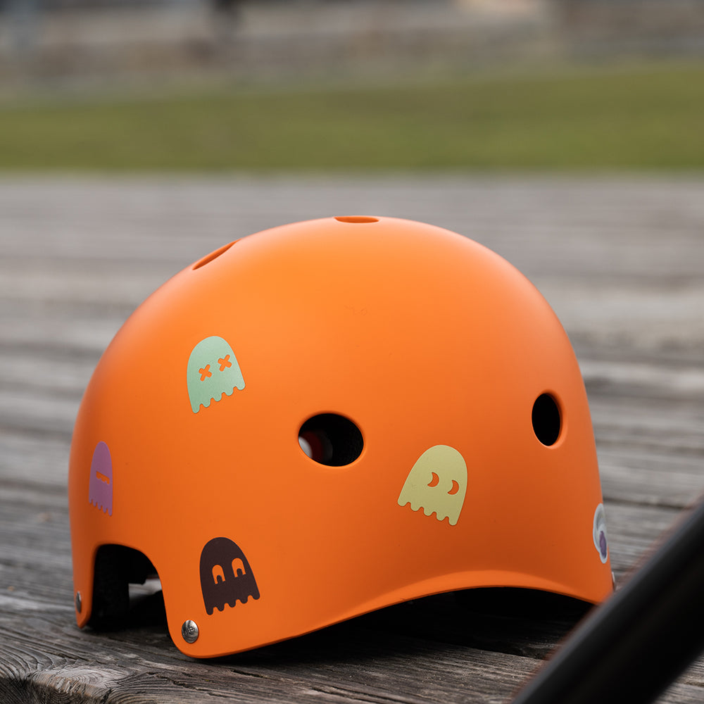 Helm orange, auf Holzboden liegend, mit bunten Geister Aufklebern verteilt