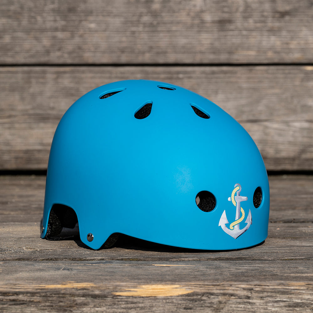 Blauer Helm liegt auf Holzboden, mit Anker Sticker vorne aufgeklebt